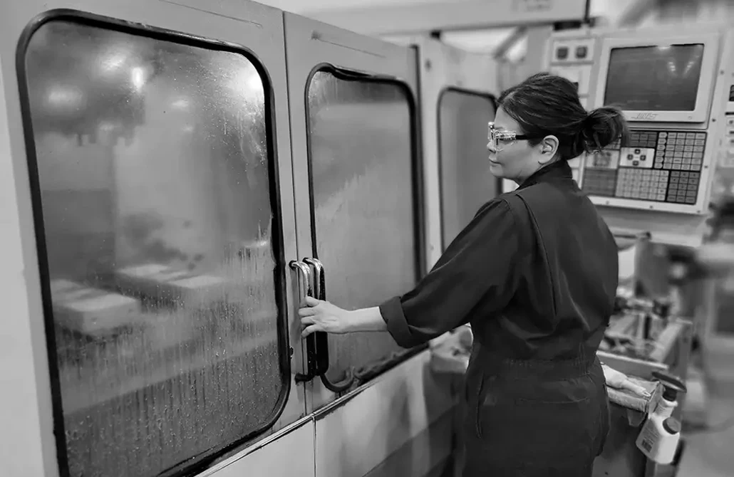 A women with safety goggles on with her hand on the door handle in black and white